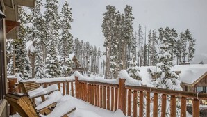 A wooden deck with snow-covered chairs and a railing, surrounded by snow-laden trees. - Spacious Ski-In/Ski-Out Retreat (Big Sky)