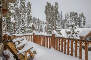 A wooden deck with snow-covered chairs and a railing, surrounded by snow-laden trees. - Spacious Ski-In/Ski-Out Retreat (Big Sky)