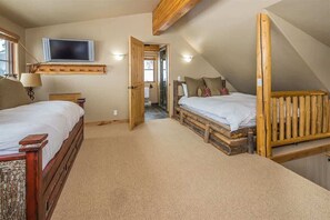 A bedroom with two beds, a TV, and a wooden ceiling.