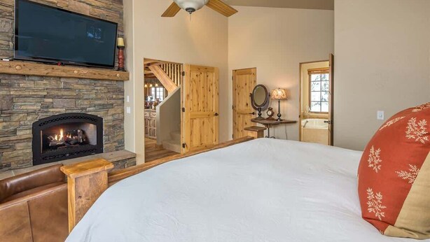 A bedroom with a fireplace, a bed, a TV, and a staircase leading to another room. - Spacious Ski-In/Ski-Out Retreat (Big Sky)