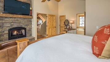 A bedroom with a fireplace, a bed, a TV, and a staircase leading to another room.