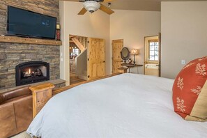 A bedroom with a fireplace, a bed, a TV, and a staircase leading to another room. - Spacious Ski-In/Ski-Out Retreat (Big Sky)