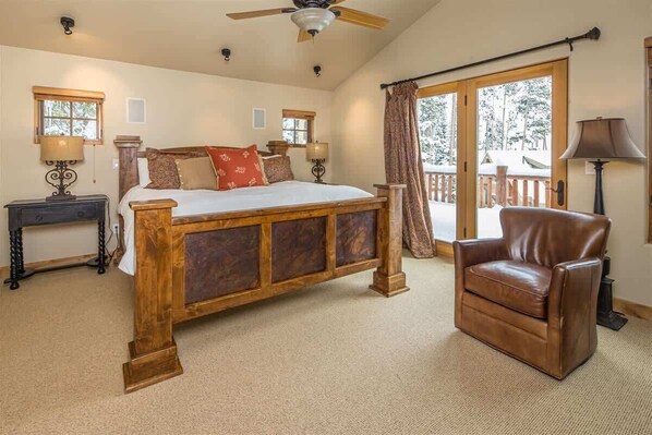 Une chambre avec un lit en bois, un fauteuil en cuir, un ventilateur de plafond et une vue sur une terrasse enneigée.