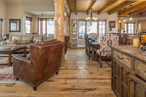 A spacious living room with a large leather sofa, a dining area with patterned chairs, and a kitchen with wooden cabinets and a bar. - Spacious Ski-In/Ski-Out Retreat (Big Sky)