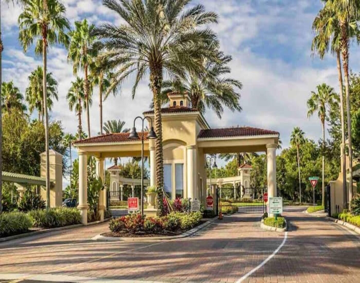 A gated entrance with a covered pavilion, palm trees, and a clear sky.