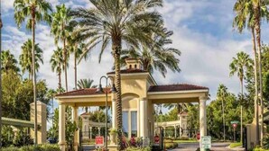 A gated entrance with a covered pavilion, palm trees, and a clear sky. - Sun Key Resort Townhouse🏝 10 min from Disney (Kissimmee)