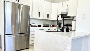 A modern kitchen with white cabinetry, a stainless steel refrigerator, a kitchen island, and a black faucet. - Sun Key Resort Townhouse🏝 10 min from Disney (Kissimmee)