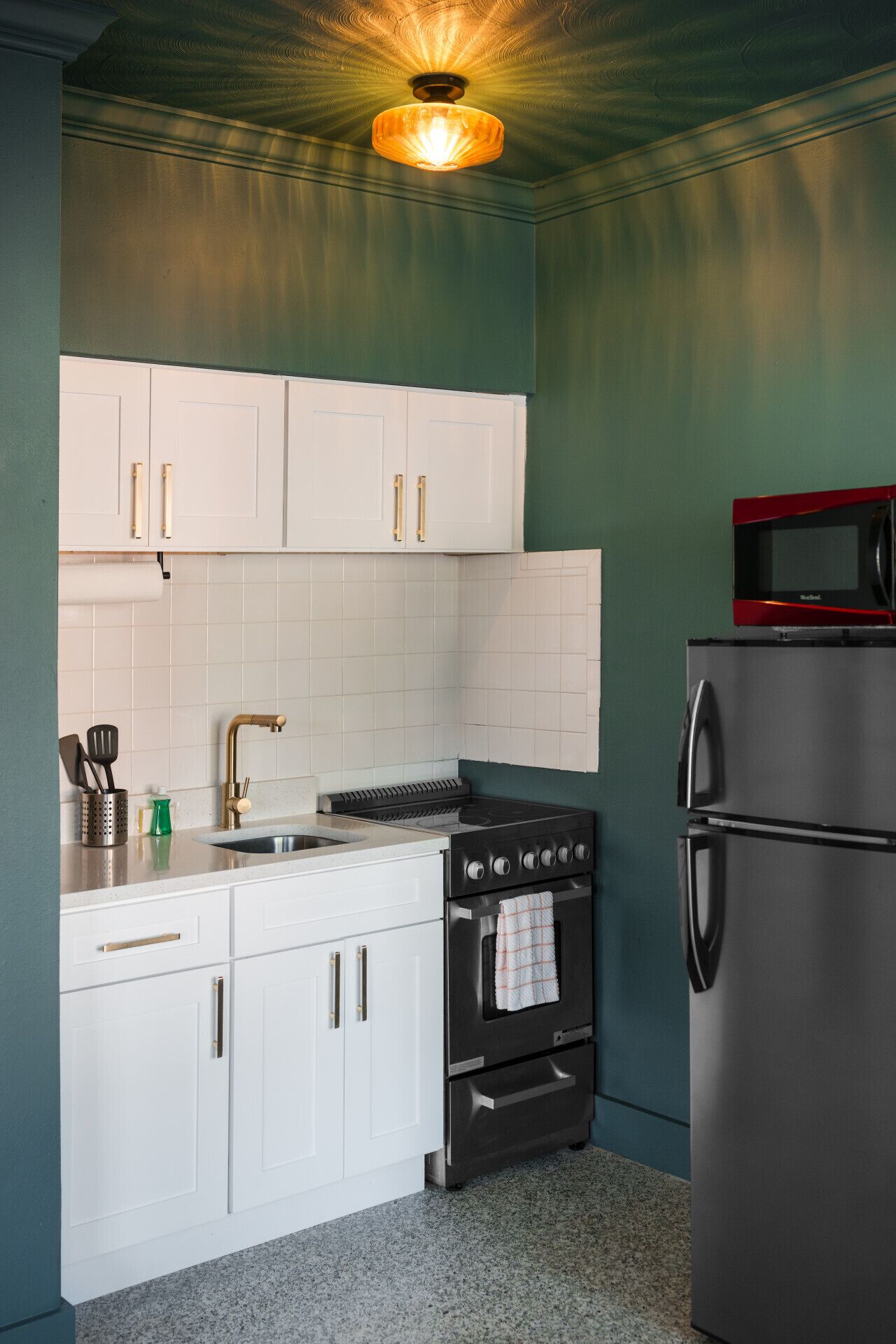 A kitchen with white cabinets, a stainless steel stove, and a black refrigerator.