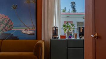 A room with a sofa, a painting, a desk with a plant, and a view through a window.