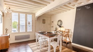 Un espace repas avec une table en bois et des chaises blanches, un tableau noir au mur et une fenêtre donnant sur des immeubles.