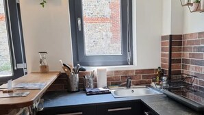 Et køkken med en murstensbagevæg, et vindue med udsigt og en vask med diverse køkkenredskaber.