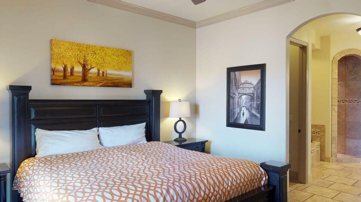 Habitación de hotel con una cama grande, una mesita de noche con lámpara y dos cuadros en las paredes.