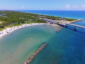 An aerial view of a beach with a pier extending into the water, surrounded by greenery and a clear blue sky. - Family Retreat on Water Spacious 4BR/4BA Getaway (Sebastian)