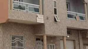 A multi-story building with balconies, a sign indicating a business, and a gated entrance. - Designer apartment (Dakar)