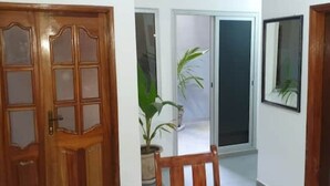 A hallway with a wooden door, a potted plant, and a framed picture on the wall. - Designer apartment (Dakar)