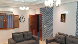 A living room with two sofas, a chandelier, a wall clock, and a door leading to another room. - Designer apartment (Dakar)