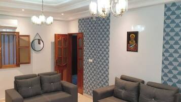 A living room with two sofas, a chandelier, a wall clock, and a door leading to another room.