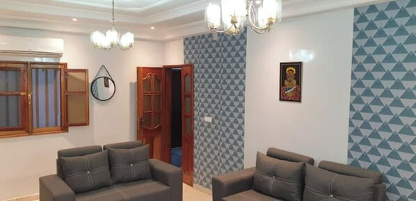 A living room with two sofas, a chandelier, a wall clock, and a door leading to another room.
