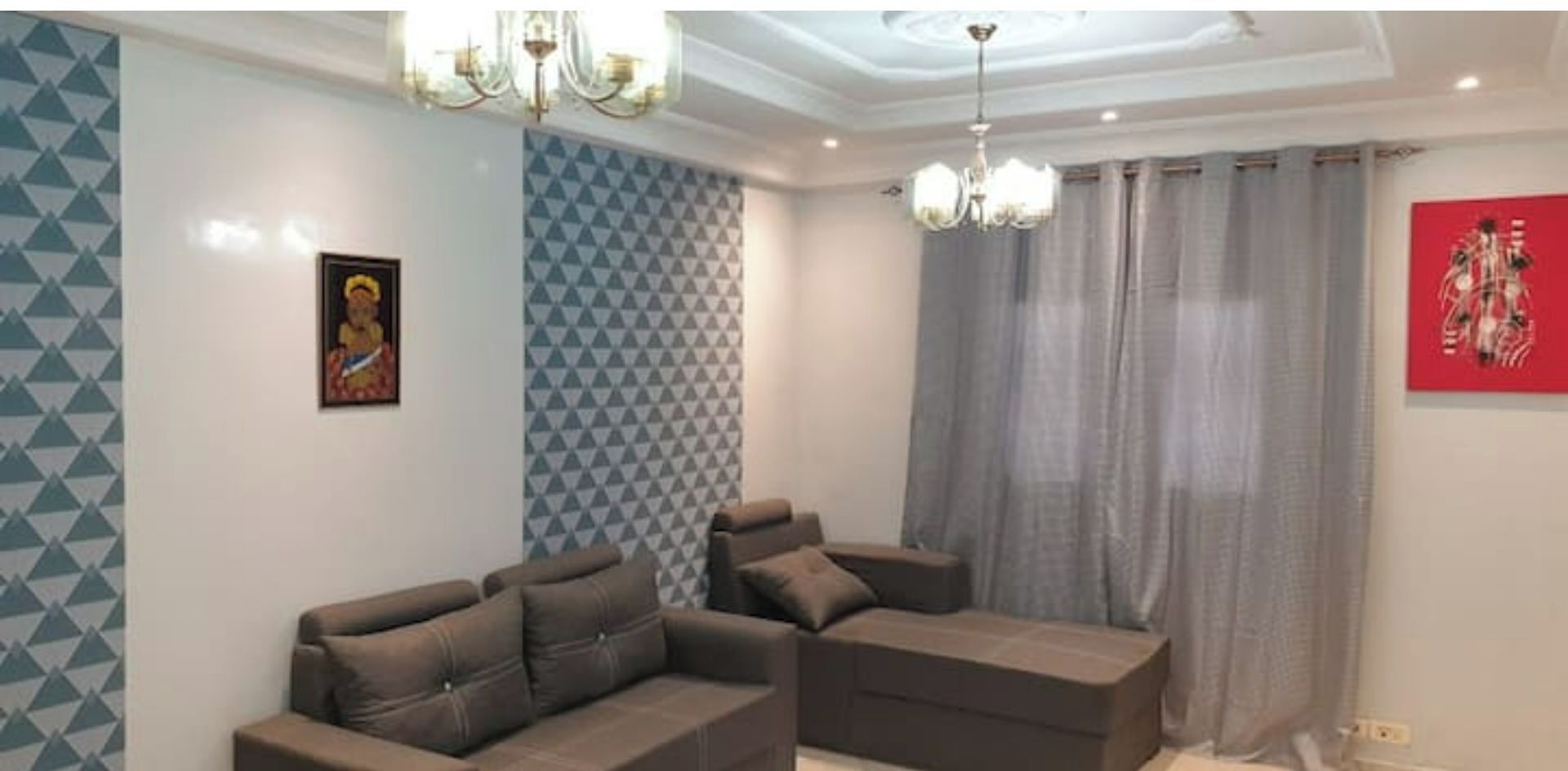 A living room with a sofa set, patterned wallpaper, a chandelier, and a red artwork on the wall.