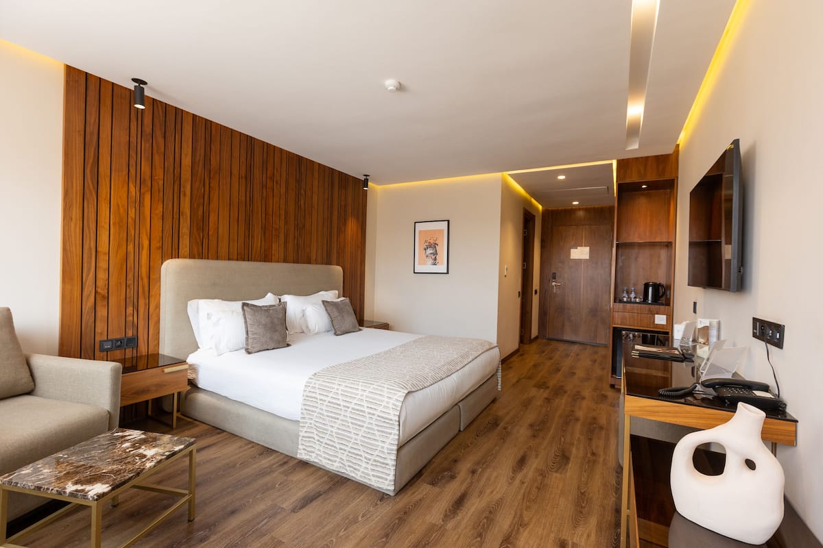 Una habitación de hotel moderna con una pared de acento de madera, una cama grande con cabecera blanca, un escritorio con televisor de pantalla plana y una pequeña zona de estar.