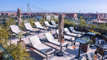 Un área de lounge en la azotea con sillones de sol, sombrillas y luces colgantes.