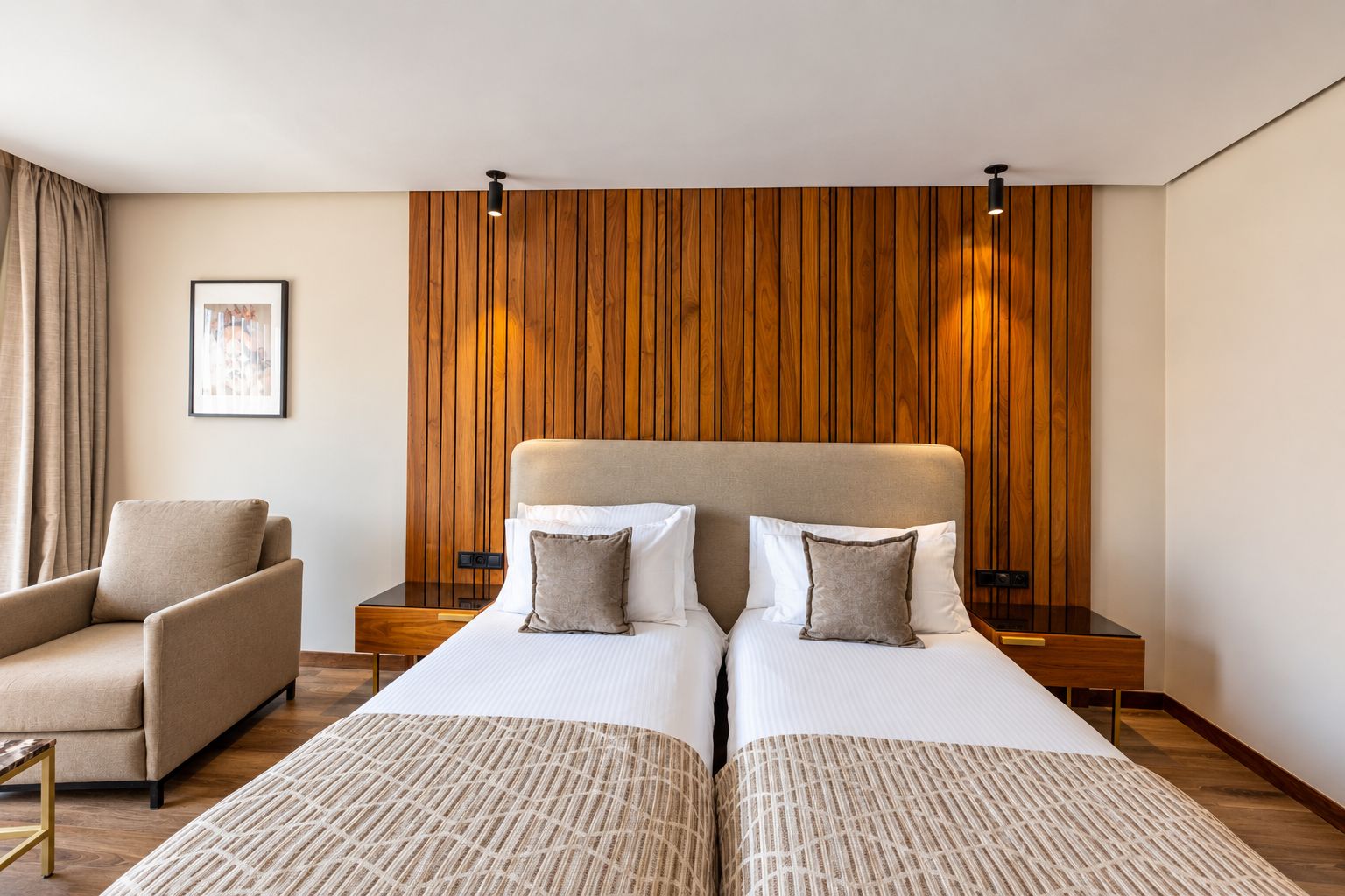 A hotel room with two beds, a sofa, wooden paneling on the wall, and a framed picture on the wall.