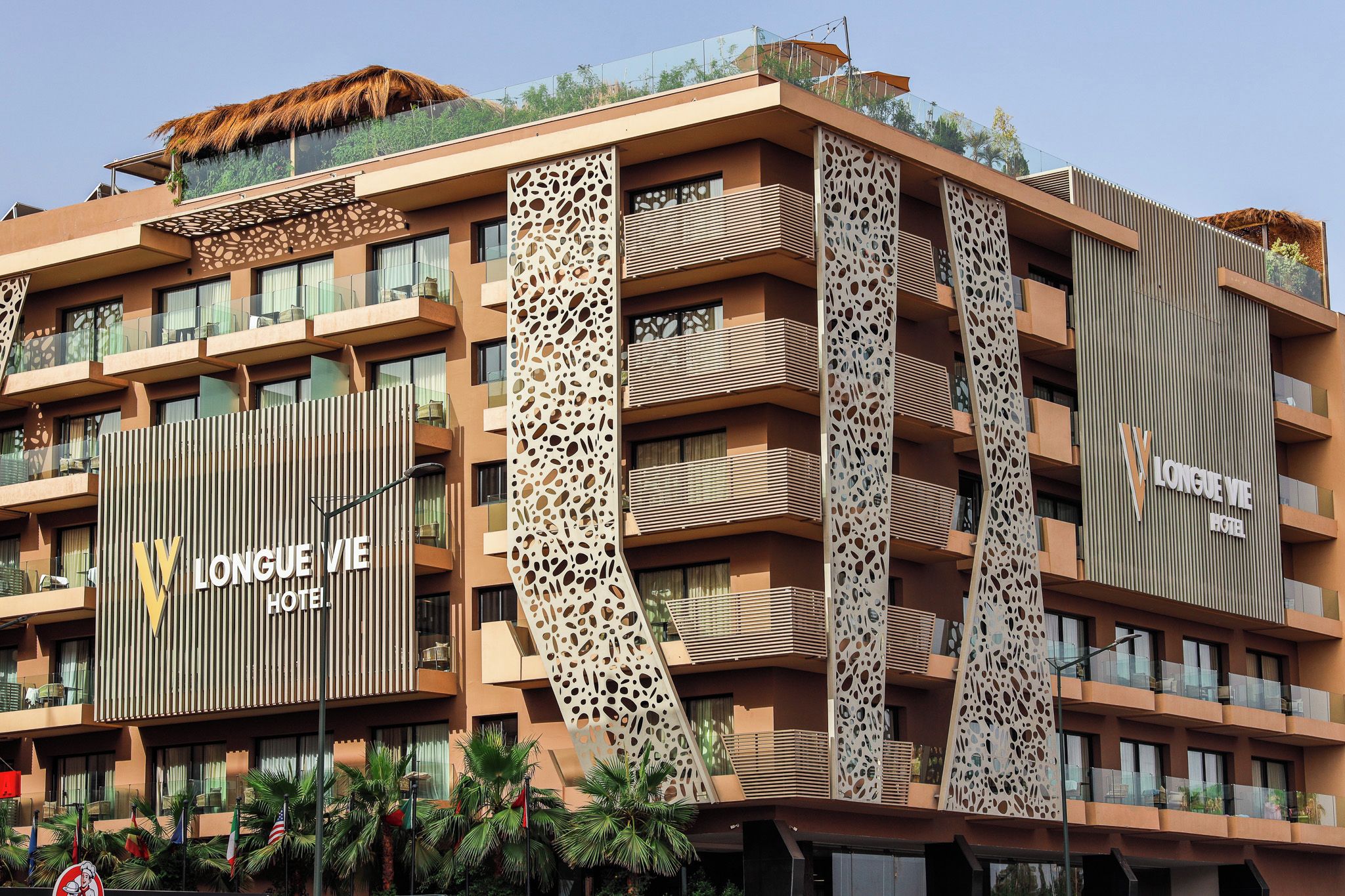 Un moderno edificio de hotel con varios balcones, una fachada distintiva con diseños recortados y un letrero que dice 'Longue Vie Hotel'.