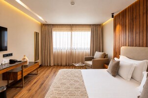 Habitación de hotel con cama, escritorio, silla, televisión y ventana con cortinas.