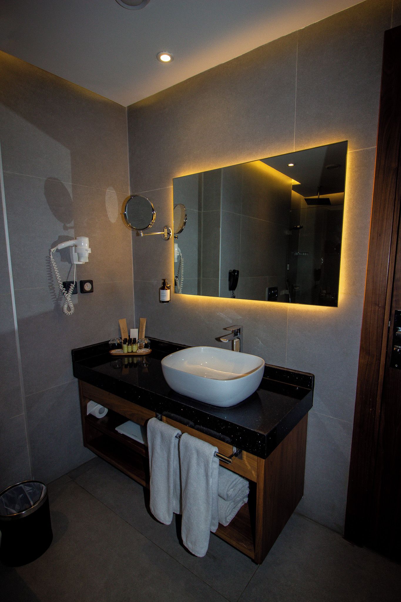 A modern bathroom with a large mirror, a white sink, and a vanity with a towel rack.