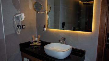A modern bathroom with a large mirror, a white sink, and a vanity with a towel rack.