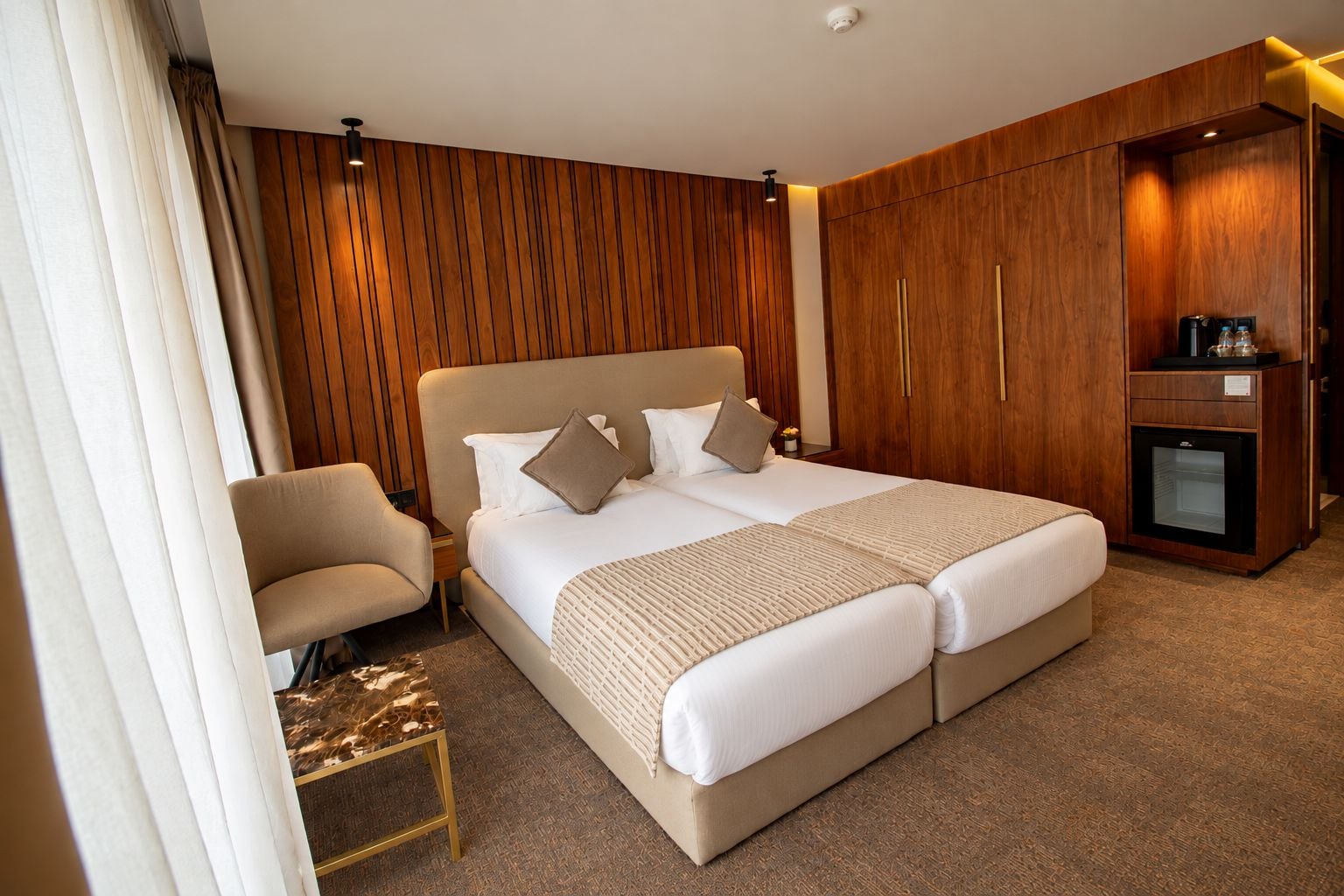 Habitación de hotel con cama doble, mesita de noche, silla, armario y minibar.