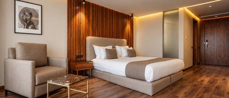 Een moderne hotelkamer met een groot bed, een zithoek met een klein tafeltje en een houten vloer.