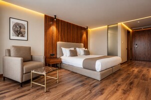 Una moderna camera d'albergo con un letto grande, un angolo salotto con un tavolino e un pavimento in legno.