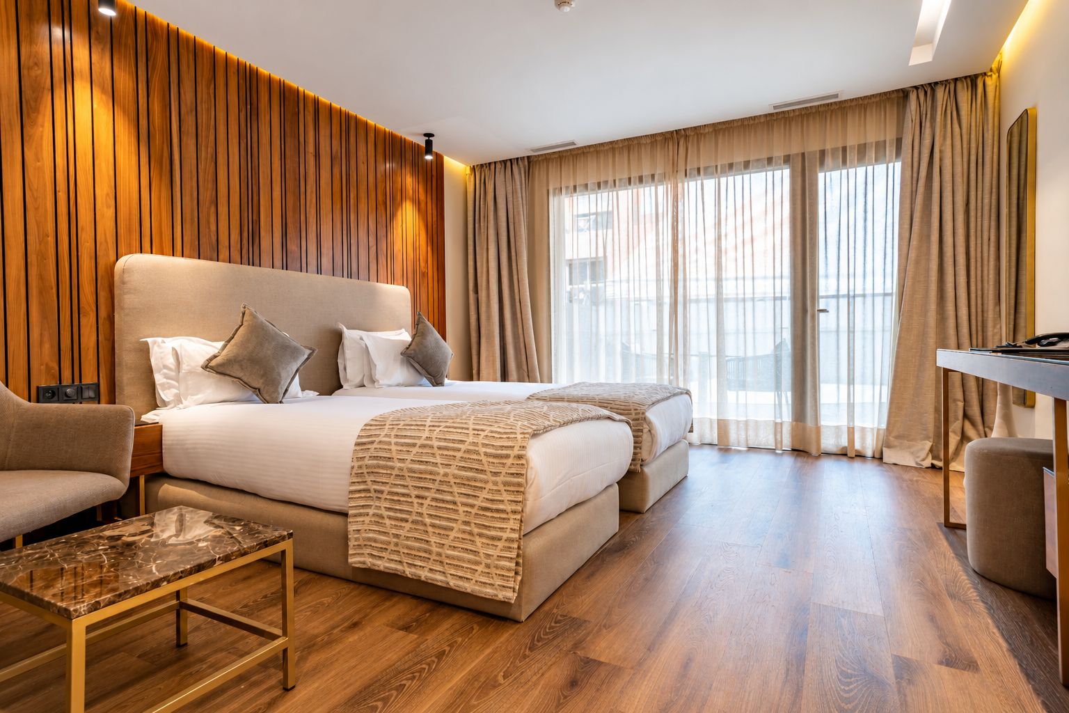 A hotel room with a large bed, a desk, and a chair. There is a window with curtains.