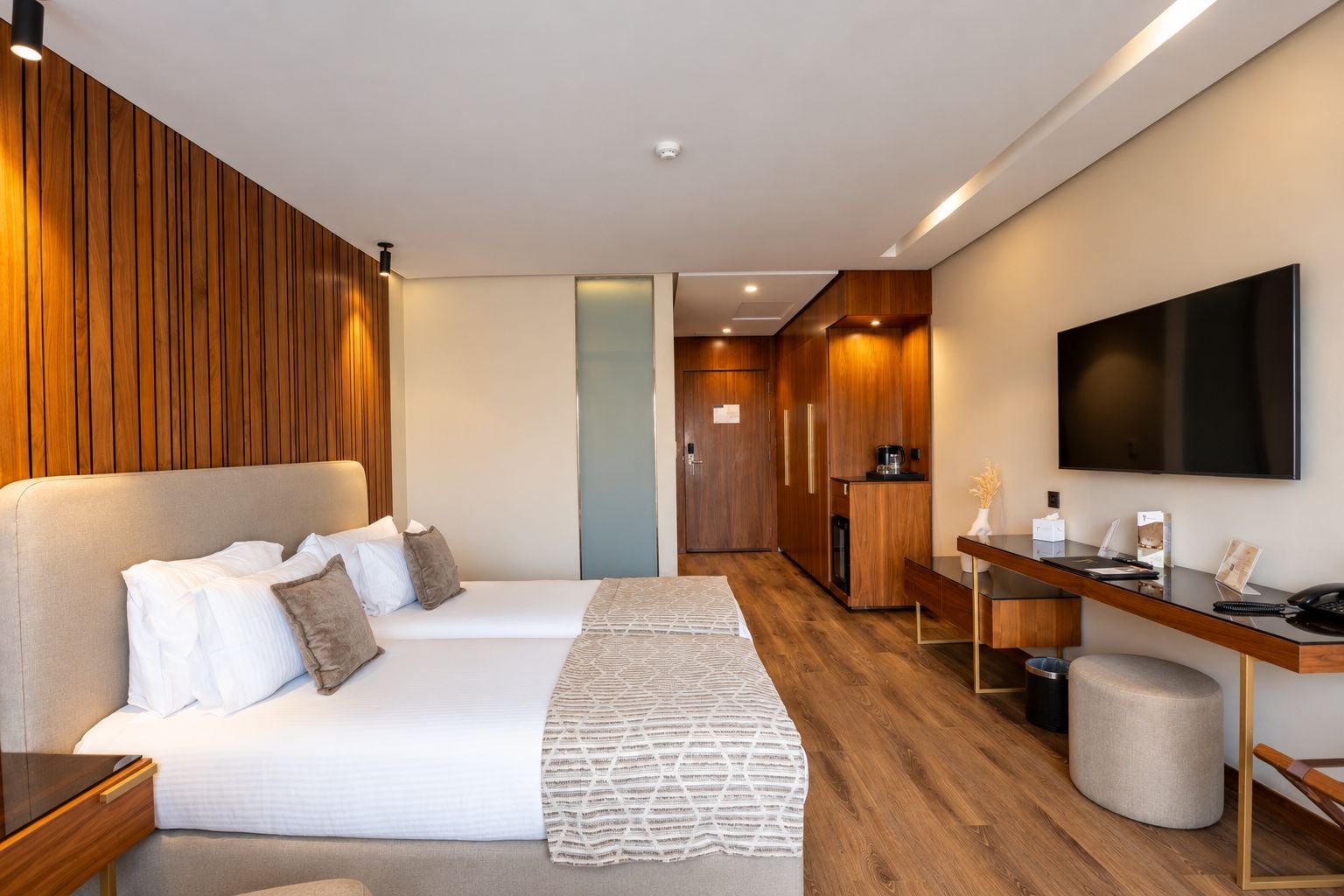 Habitación de hotel con cama, mesita de noche, escritorio, silla y televisor montado en la pared.