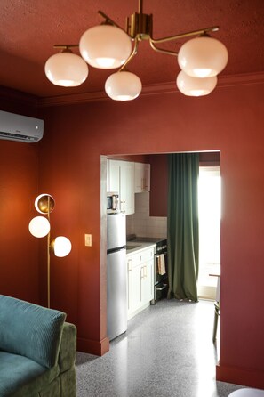 Un espace de vie compact comprenant un coin cuisine, un luminaire au plafond et un rideau vert.