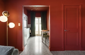 Un couloir avec une porte rouge, un coin cuisine comprenant une table et des chaises, et un luminaire sur le côté gauche.