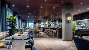 A modern restaurant with wooden tables and chairs, large windows, and hanging pendant lights. - Clarion Hotel Umea (Umea)