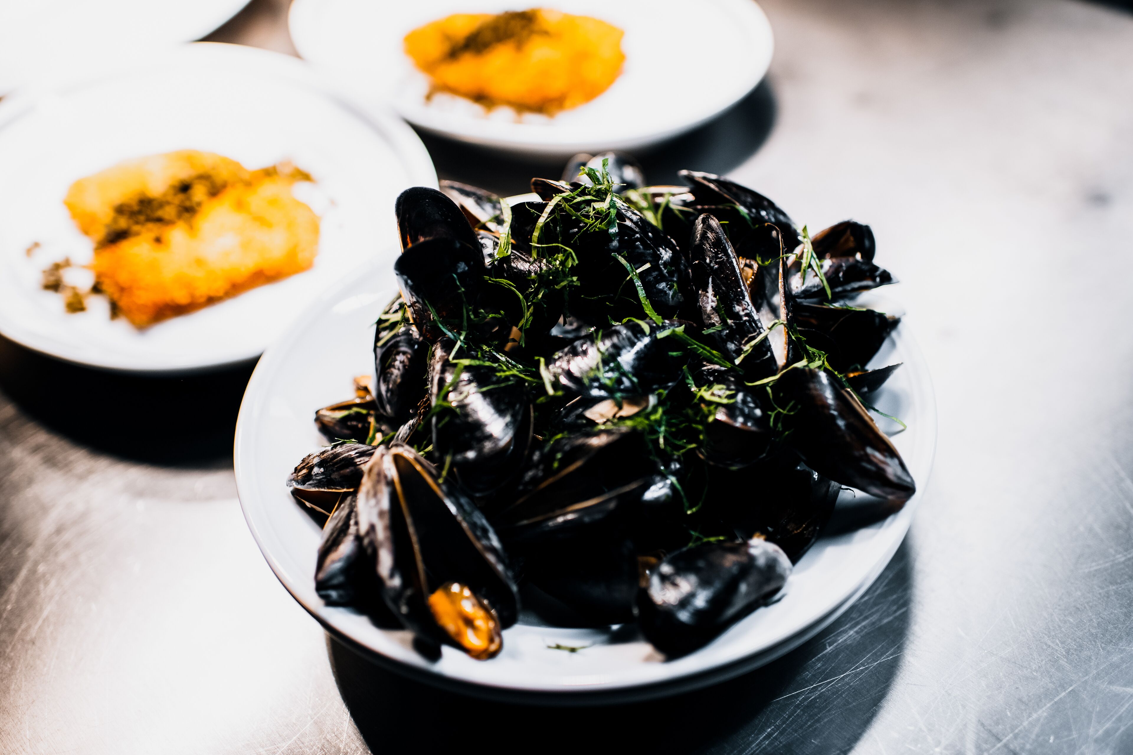 Un bol de mejillones adornados con hierbas, y otro plato al fondo.