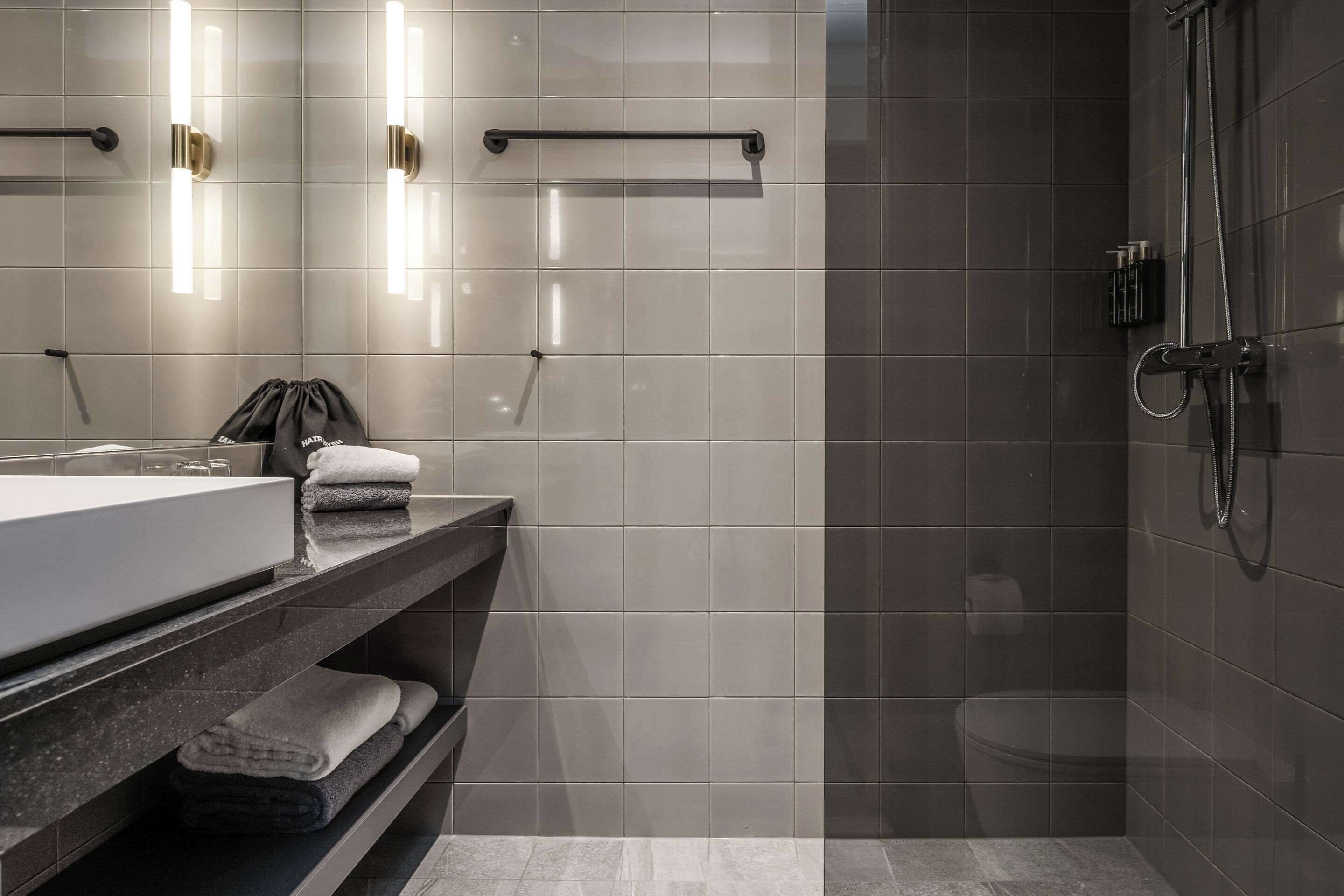 A modern bathroom with a large mirror, a sink, a towel rack, and a shower area.