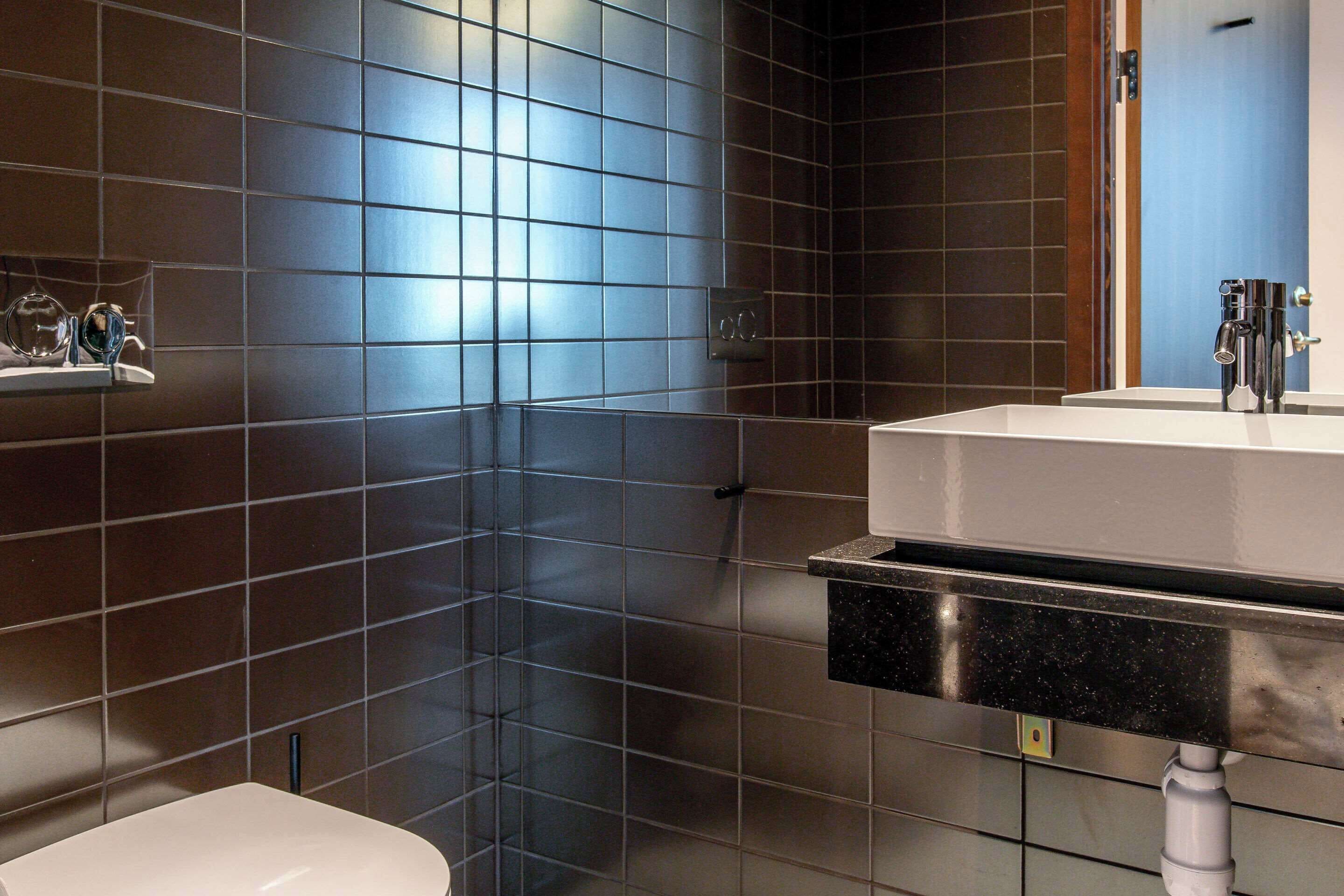 Un baño moderno con paredes de baldosas oscuras, un lavamanos blanco y un inodoro.