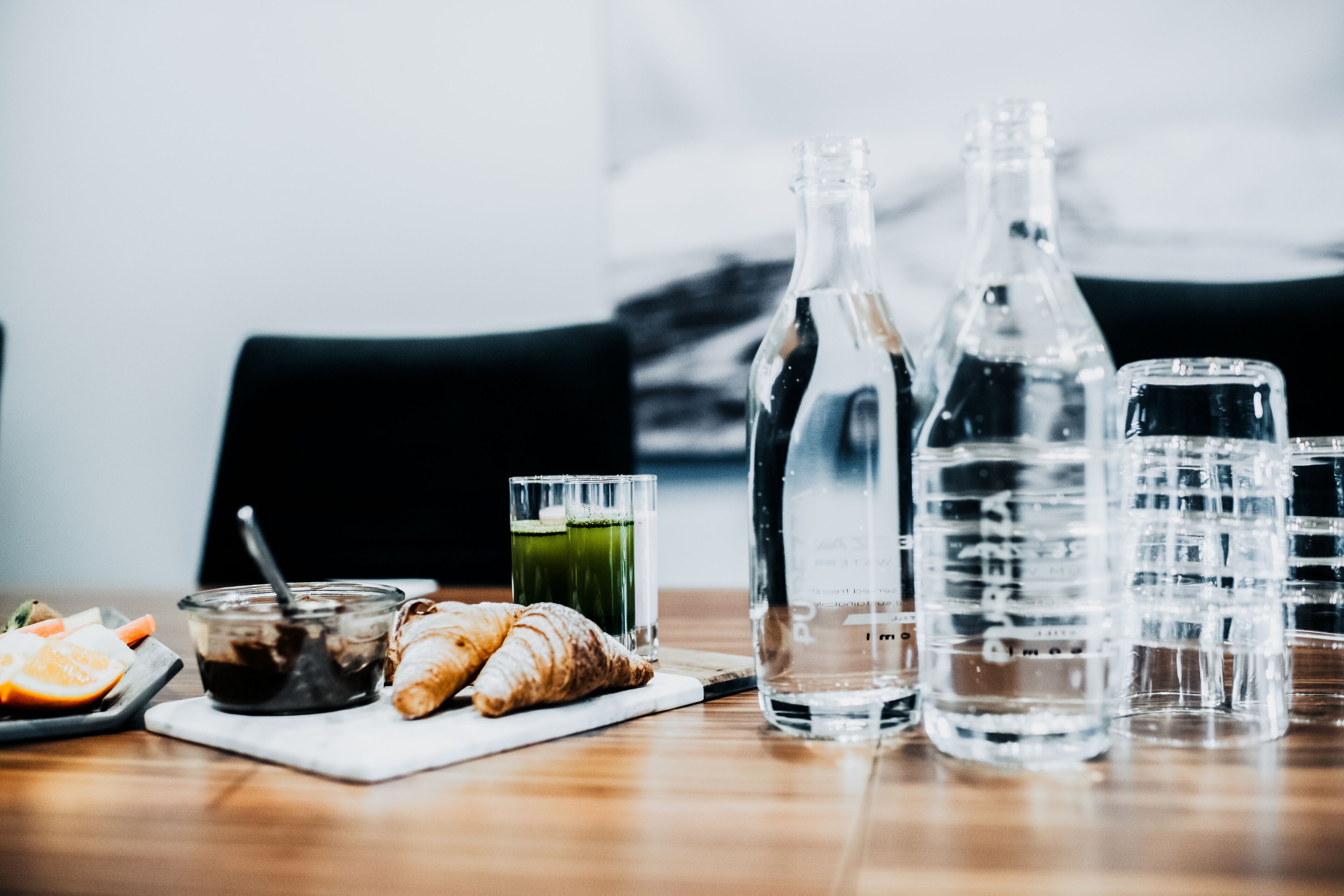 A table with a glass of juice, a bottle of water, a glass of water, a croissant, and a plate with food items.