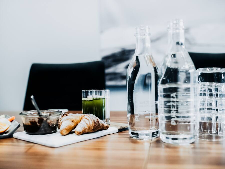 A table with a glass of juice, a bottle of water, a glass of water, a croissant, and a plate with food items.