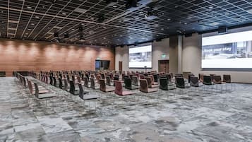 Konferenssihuone, jossa on riveissä tuoleja, suuri näyttö ja projektori.