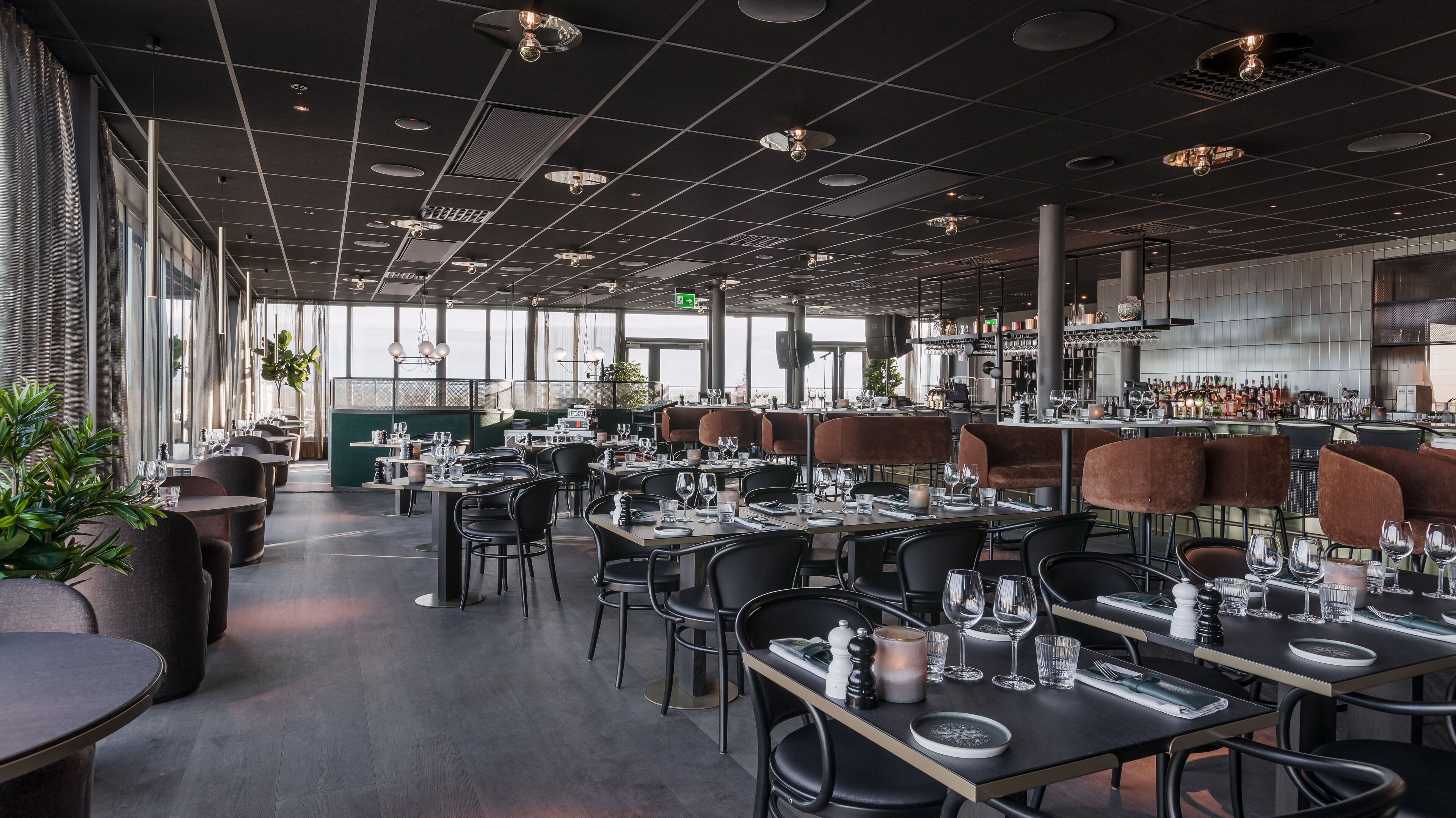 A modern restaurant with a long counter, black chairs, and a bar area.