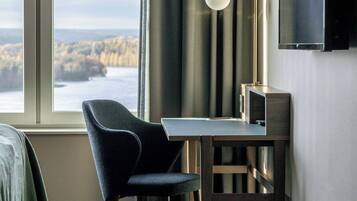 A modern room with a view of a body of water, a desk with a chair, a lamp, and a flat-screen TV mounted on the wall.