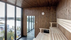 A modern room with wooden panel walls, large windows offering a view of a river and buildings, and a bench with a small trash bin. - Clarion Hotel Umea (Umea)