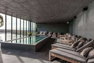 Zona de piscina interior moderna con sillones de descanso y vistas al exterior.