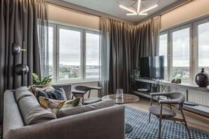 A modern living room with a sofa, chairs, a TV, and large windows offering a city view. - Clarion Hotel Umea (Umea)