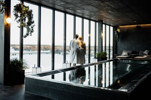 A couple standing by a large indoor pool with a view of a snowy landscape through large windows. - Clarion Hotel Umea (Umea)